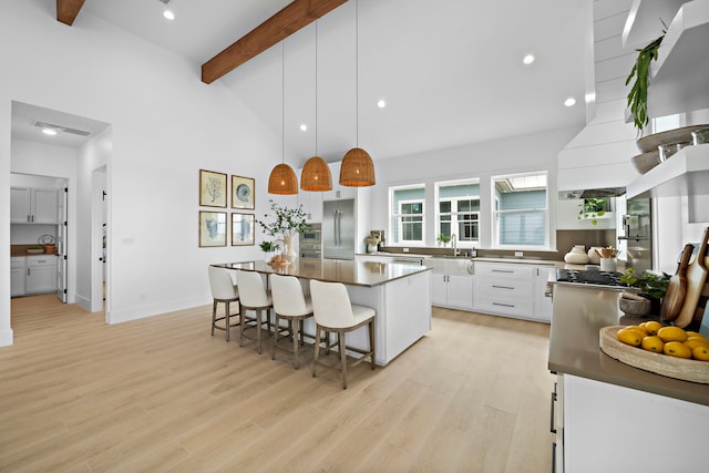 kitchen with a breakfast bar, stainless steel built in fridge, beamed ceiling, a sink, and light wood-type flooring