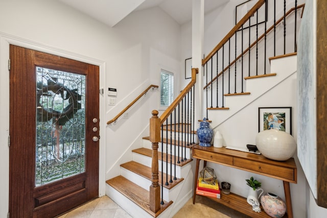 entrance foyer with light tile patterned flooring, stairway, and a towering ceiling