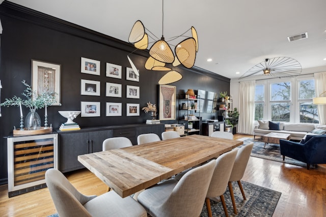 dining space with wine cooler, ornamental molding, light wood finished floors, and visible vents