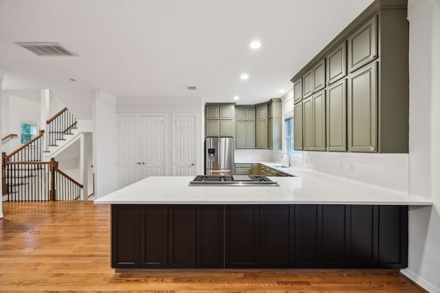 kitchen featuring a sink, light countertops, light wood finished floors, a peninsula, and stainless steel appliances