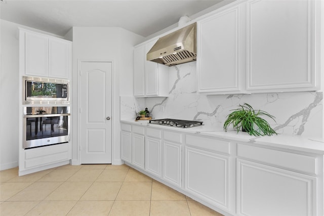 kitchen with under cabinet range hood, light tile patterned floors, tasteful backsplash, white cabinetry, and appliances with stainless steel finishes