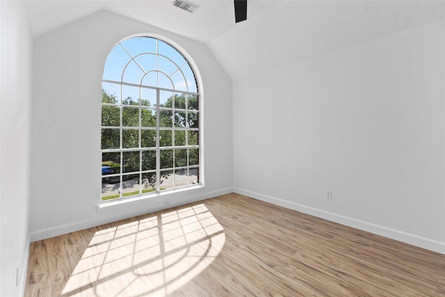 empty room featuring visible vents, baseboards, vaulted ceiling, wood finished floors, and a ceiling fan
