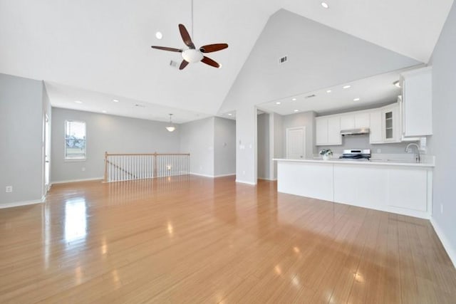 unfurnished living room with light wood-style flooring, visible vents, baseboards, a ceiling fan, and high vaulted ceiling