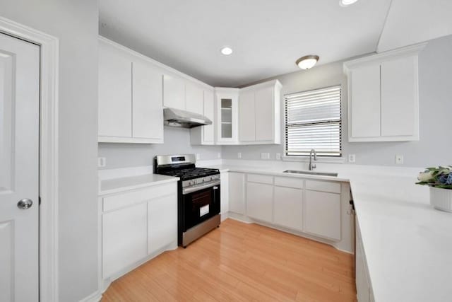 kitchen with a sink, stainless steel range with gas stovetop, under cabinet range hood, white cabinetry, and light countertops