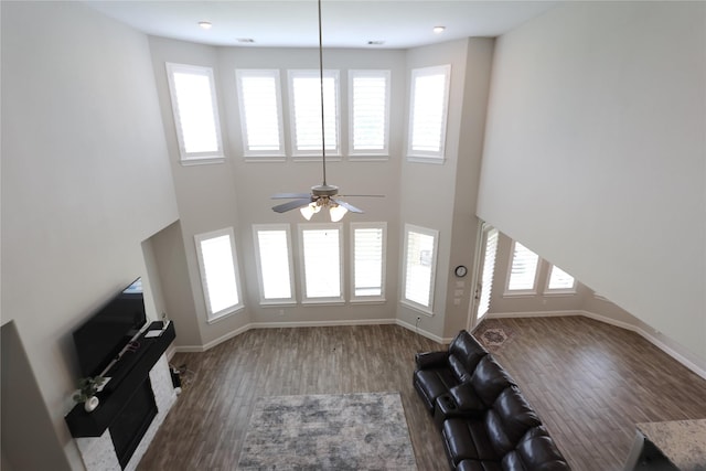 unfurnished living room with baseboards, a ceiling fan, a high ceiling, and wood finished floors