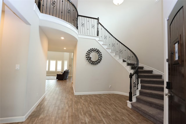 foyer featuring a towering ceiling, wood finished floors, baseboards, stairway, and recessed lighting