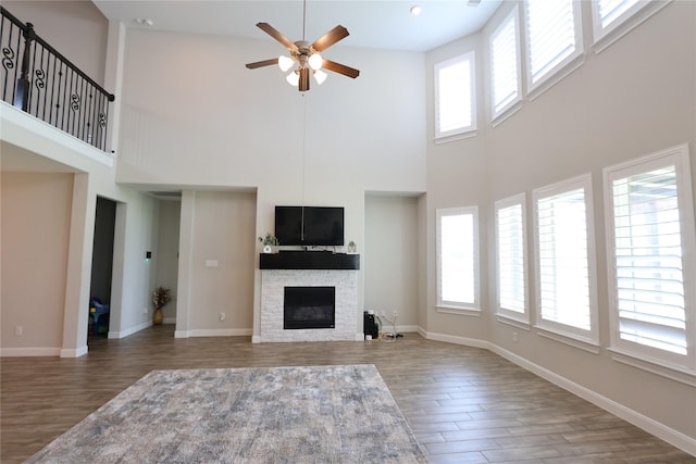unfurnished living room with a high ceiling, a fireplace, a ceiling fan, baseboards, and wood finished floors