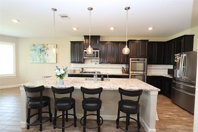 kitchen featuring backsplash, visible vents, appliances with stainless steel finishes, a sink, and light stone counters