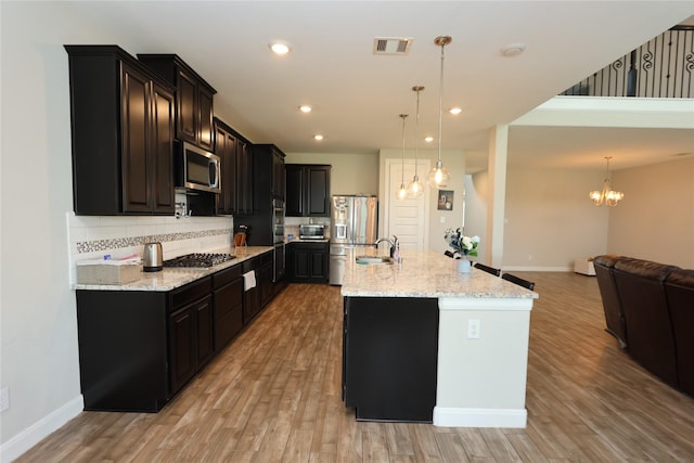 kitchen with a sink, light wood finished floors, stainless steel appliances, decorative backsplash, and visible vents