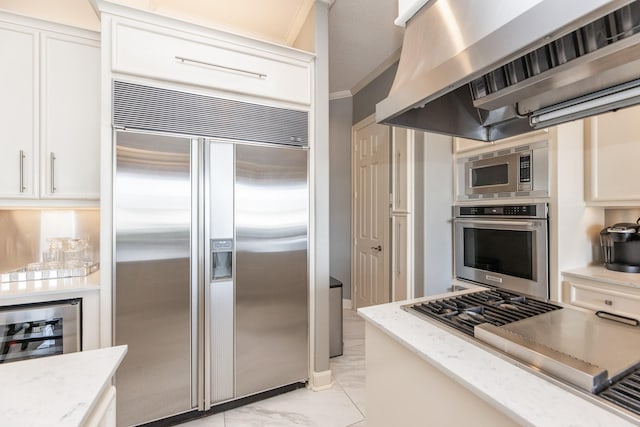 kitchen featuring white cabinets, built in appliances, beverage cooler, light stone countertops, and ventilation hood