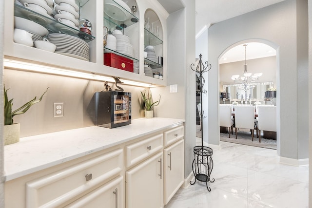 bar featuring marble finish floor, a notable chandelier, baseboards, and arched walkways