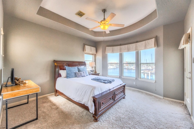 bedroom with light colored carpet, visible vents, a tray ceiling, and multiple windows