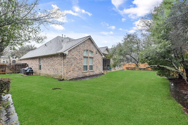 view of side of home featuring brick siding, a yard, a fenced backyard, central AC, and roof with shingles