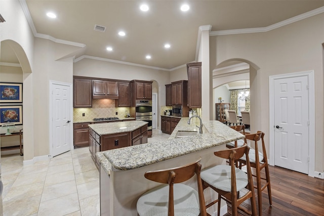 kitchen featuring arched walkways, decorative backsplash, appliances with stainless steel finishes, a kitchen island, and a sink