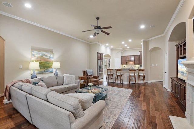 living area with dark wood-type flooring, ceiling fan, crown molding, and arched walkways
