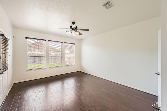 unfurnished room featuring visible vents, a ceiling fan, dark wood finished floors, and baseboards