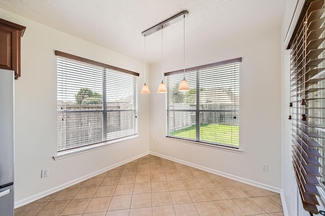 unfurnished dining area with baseboards, a textured ceiling, light tile patterned floors, and a wealth of natural light