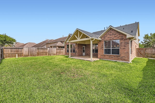 rear view of property with brick siding, a fenced backyard, a patio area, and a lawn
