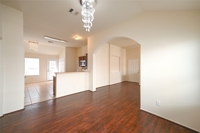 unfurnished living room with lofted ceiling, visible vents, arched walkways, an inviting chandelier, and wood finished floors