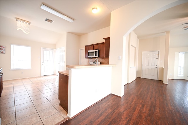 kitchen with lofted ceiling, stainless steel microwave, light countertops, a peninsula, and backsplash