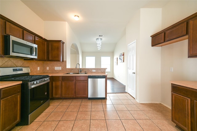 kitchen with tasteful backsplash, appliances with stainless steel finishes, light countertops, a sink, and a peninsula
