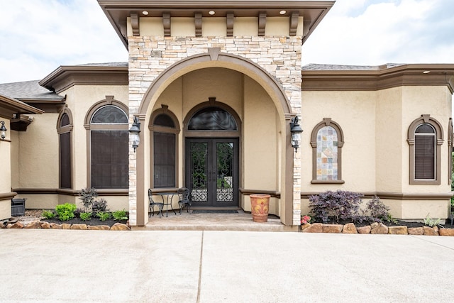 view of exterior entry featuring french doors, stucco siding, and stone siding