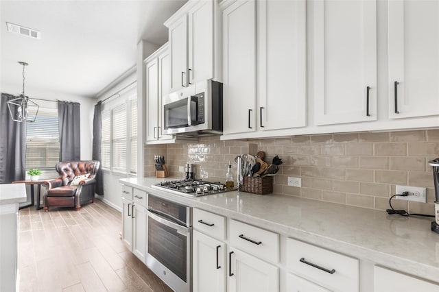 kitchen with decorative backsplash, light wood-style floors, light stone counters, white cabinetry, and appliances with stainless steel finishes