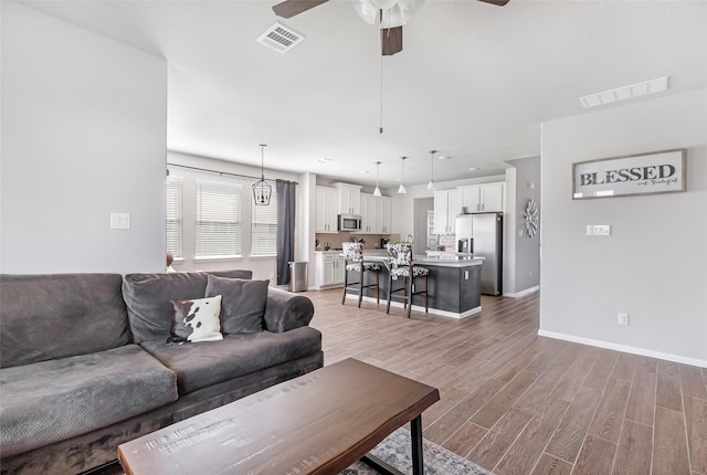 living area with baseboards, visible vents, ceiling fan, and light wood-style floors