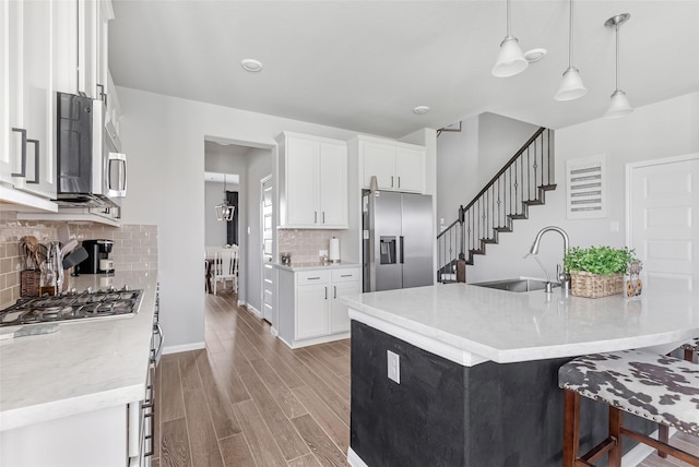 kitchen with appliances with stainless steel finishes, white cabinets, a sink, light wood-type flooring, and a kitchen breakfast bar