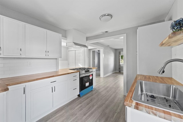 kitchen with stainless steel gas range, a sink, tasteful backsplash, white cabinetry, and wooden counters