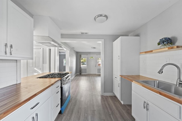kitchen with a sink, visible vents, wooden counters, stainless steel gas range, and backsplash