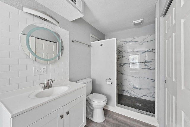 bathroom with vanity, toilet, a marble finish shower, visible vents, and wood finished floors