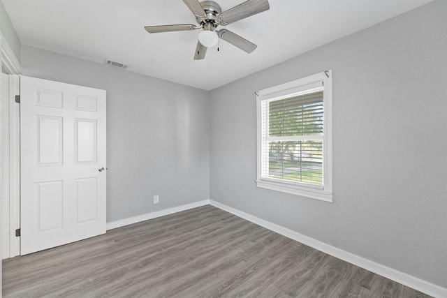 empty room with wood finished floors, visible vents, ceiling fan, and baseboards