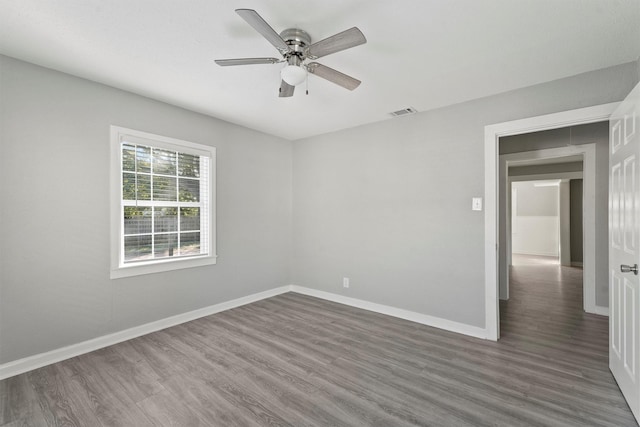 spare room featuring wood finished floors, a ceiling fan, visible vents, and baseboards