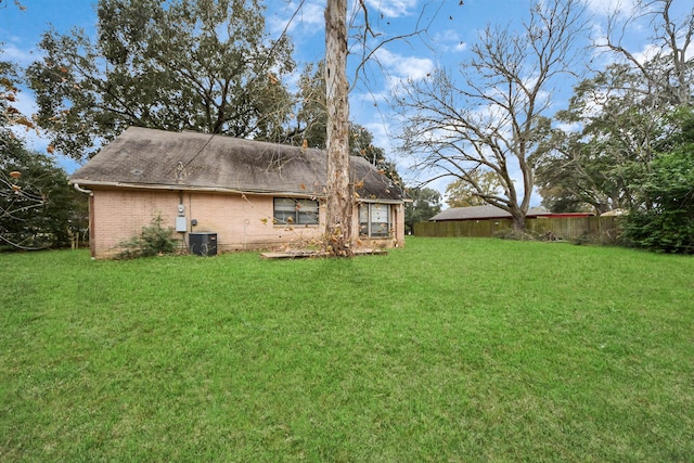 back of property with brick siding, cooling unit, a lawn, roof with shingles, and fence