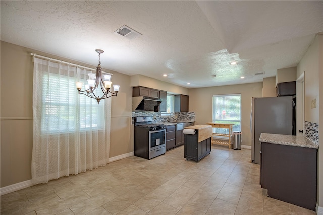 kitchen featuring a chandelier, stainless steel appliances, a kitchen island, wall chimney exhaust hood, and backsplash