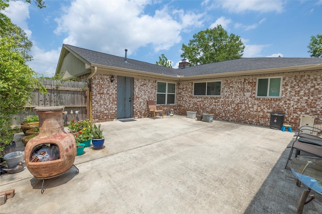 back of house with a chimney, brick siding, fence, a shingled roof, and a patio