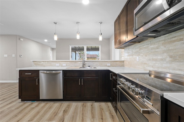 kitchen featuring a sink, stainless steel appliances, tasteful backsplash, a peninsula, and light wood-style flooring