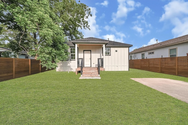 back of property with a fenced backyard, board and batten siding, a lawn, and a shingled roof