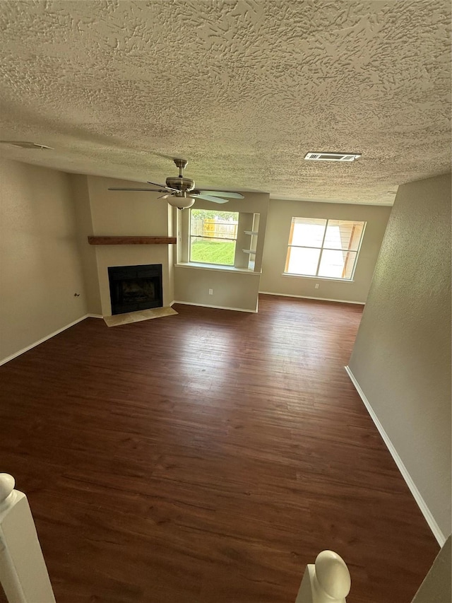 unfurnished living room featuring a textured ceiling, ceiling fan, dark wood-style floors, baseboards, and a fireplace