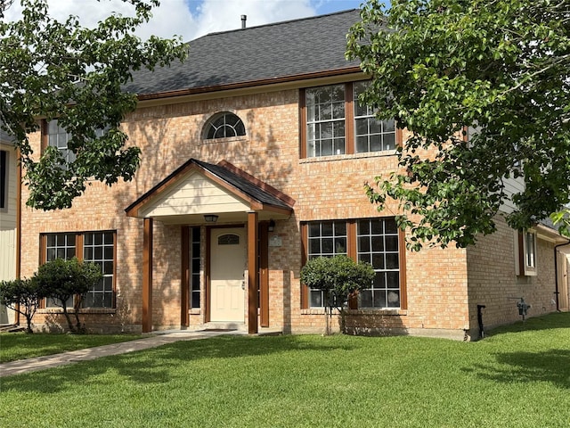 view of front of home featuring brick siding, a front lawn, and roof with shingles