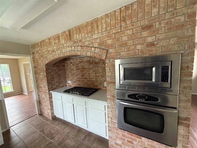 kitchen with white cabinets, dark tile patterned flooring, appliances with stainless steel finishes, and brick wall