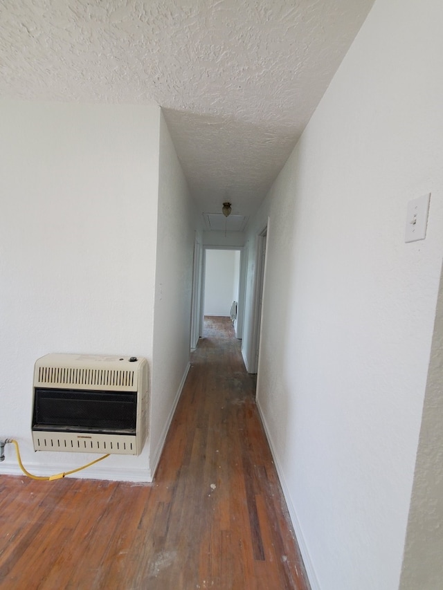 hall with attic access, heating unit, baseboards, a textured ceiling, and hardwood / wood-style flooring