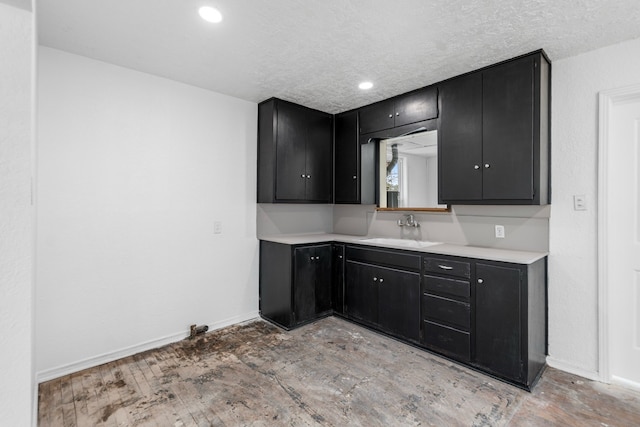 kitchen with light countertops, a sink, dark cabinets, and baseboards
