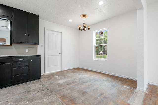 unfurnished dining area featuring recessed lighting, a textured ceiling, a chandelier, and baseboards