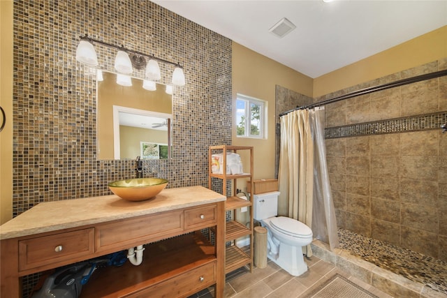 bathroom featuring a tile shower, vanity, toilet, tile walls, and visible vents