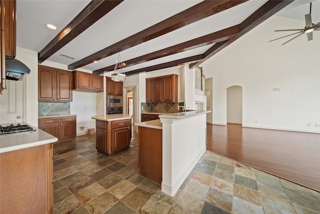 kitchen featuring decorative backsplash, a ceiling fan, appliances with stainless steel finishes, arched walkways, and beamed ceiling