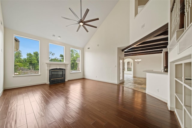unfurnished living room featuring a glass covered fireplace, wood finished floors, baseboards, high vaulted ceiling, and ceiling fan with notable chandelier
