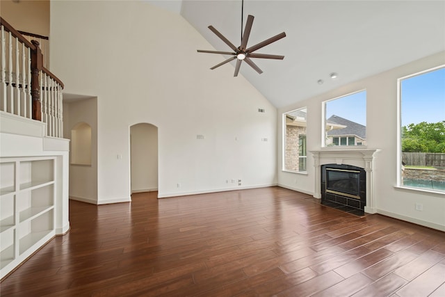 unfurnished living room featuring a ceiling fan, arched walkways, a tile fireplace, wood finished floors, and high vaulted ceiling