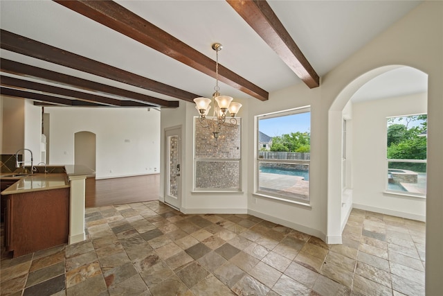 unfurnished dining area featuring a healthy amount of sunlight, baseboards, beam ceiling, and stone tile floors